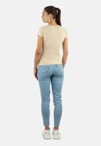 Beige eng anliegendes T-Shirt mit kurzen Ärmeln, kombiniert mit hellblauen Skinny-Jeans und weißen Sneakers. Hinweis: sichtbare Nähte an Rücken und Seiten.