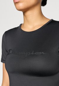 Μαύρο εφαρμοστό T-shirt από λείο ύφασμα, με ματ μαύρο λογότυπο "Champion" στο στήθος και στρογγυλή λαιμόκοψη.