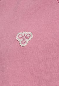 Wit geborduurd bijenlogo op roze gestructureerde stof, gecentreerd en duidelijk zichtbaar.