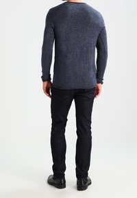 Dunkelgrauer gestrickter Pullover mit Rundhalsausschnitt, langen Ärmeln und strukturiertem Finish, kombiniert mit dunklen Jeans und schwarzen Schuhen.