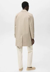 Beige Trenchcoat aus Baumwolle, mit gerader Silhouette, leicht oversized Passform, Knopfmanschetten und einem Schlitz auf der Rückseite.