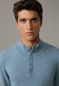 Pullover blu lavorato a maglia con colletto alto e pattina con bottoni. Texture morbida con un sottile motivo melangiato, design aderente.