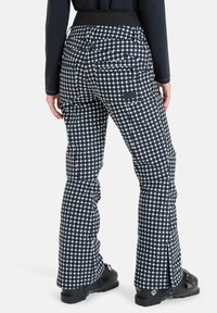 Granatowe i białe spodnie narciarskie w wzór w kropki, z czarnym pasem w talii i zamkami błyskawicznymi przy kostkach. Widoczne wiele kieszeni z tyłu.