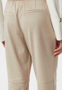 Beige, samtartige maßgeschneiderte Hosen mit Gesäßtaschen und entspanntem Schnitt. Die glatte Textur und dezente Steppdetails werten das Design auf.