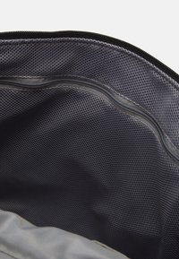 Bolsa de tela gris con un interior texturizado y un bolsillo con cremallera. Presenta un forro de malla visible y un color sólido.