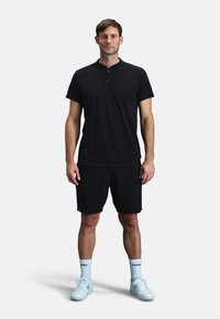 T-shirt de sport noir avec un col court, associé à un short noir. La chaussure est des baskets bleu clair, avec des chaussettes blanches portant le logo Kempo.