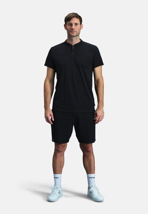 Sort sports T-shirt med kort krave, parret med sorte shorts. Fodtøj er lyseblå sneakers med hvide sokker, der har Kempo-logo.