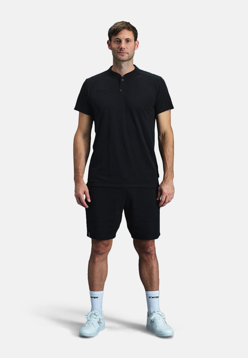 T-shirt de sport noir avec un col court, associé à un short noir. La chaussure est des baskets bleu clair, avec des chaussettes blanches portant le logo Kempo.