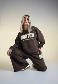 Brun sweatshirt med texten "BOSTON" och "CITY OF MASSACHUSETTS", ihop med matchande löst sittande byxor med mjukt material och vida ben.