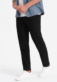 Pantalons noirs fuselés avec une texture lisse, associés à des baskets blanches. La tenue comprend une chemise à boutons bleu clair.