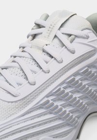 Λευκό αθλητικό παπούτσι με υφασμένο πάνω μέρος από πλέγμα, ενισχυμένη σόλα με ανάγλυφα σχέδια και λευκά κορδόνια περασμένα μέσα από ενισχυμένες τρύπες.