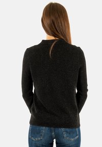 Pullover nero con una finitura testurizzata e lucente, maniche lunghe e scollatura a girocollo, indossato con jeans blu visibili in vita.