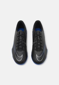 Zapatos de fútbol negros con parte superior sintética texturizada, con acentos azules y un swoosh blanco, seis ojales y un diseño de punta redondeada.