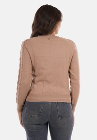 Maglione in maglia marrone chiaro con orlo a coste e dettagli a trecce sulle maniche. Presenta un piccolo logo metallico sul retro del collo.