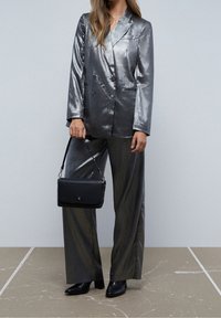 Metallic sølv blazer med dobbelt bryst design, matchende brede bukser og en sort crossbody taske. Glat tekstur, strømlinet silhuet.