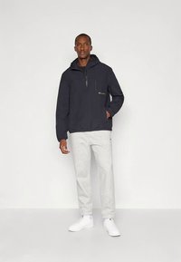 Tumesinine kapuutsiga pullover-tagi poole luku ja elastse äärega; kombineeritud helesiniste dressipükstega ja valgete tossudega. Jakil peen logo detail.