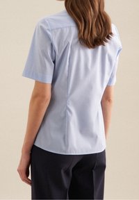 Ljusblå kortärmad skjorta med en skräddarsydd passform, med en slät yta och en något rundad nederkant, kombinerad med mörka byxor.