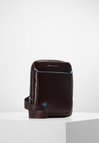 Borsa in pelle marrone di forma rettangolare, con cuciture blu a contrasto, tracolla regolabile e chiusura con zip nella parte superiore.