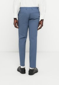 Στενά μπλε παντελόνια από λείο ύφασμα, με δύο πίσω τσέπες, φορεμένα με μαύρα παπούτσια και λευκές κάλτσες.