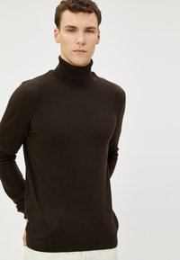 Brązowy sweter z golfem o długich rękawach, wykonany z miękkiego, gładkiego materiału. Charakteryzuje się dopasowanym krojem oraz ściągaczami przy mankietach i u dołu.