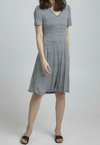 Kortärmad klänning med v-ringning i svart och vitt geometriskt mönster. Viddkjol, mjuk textur, knälång. Bärs med svarta slide-sandaler.