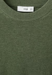 Detailný záber na olivovo zelený pletený sveter so žebrovaným okrúhlym výstrihom a bielou veľkostnou etikietou označenou MNG, EU M, USA M, MEX M.