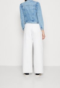 Světle modrá džínová bunda s nabíranými rukávy, bílé kalhoty širokých nohavic a námořnické tenisky. Na kalhotách jsou vidět zadní kapsy.