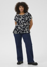 Top nera con stampa floreale, maniche corte, veste comodo, abbinato a jeans a gamba larga blu scuro e scarpe con plateau nere.