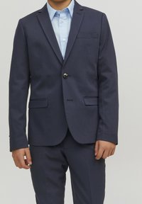 Chaqueta de traje azul marino con cierre de un solo botón, solapas con muesca y dos bolsillos delanteros; combinada con una camisa abotonada de color azul claro debajo.