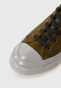 Zelené plátené tenisky s šedou gumovou špičkou, tmavými šnúrkami a kovovými očkami; majú textúrovanú látku a podrážku s diamantovým vzorom.