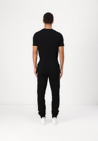 Schwarzes T-Shirt mit kurzen Ärmeln und schwarze Jogginghose mit elastischem Bund und Bündchen, kombiniert mit weißen Turnschuhen, von hinten gesehen.