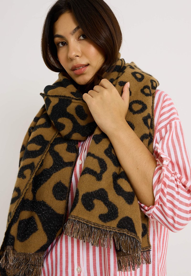 Bufanda de estampado de leopardo marrón con patrones negros, terminada con bordes desflecados y un sutil brillo. Llevada de forma holgada alrededor del cuello.