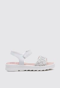 Sandalias blancas con suela texturizada, diseñadas con patrones florales perforados en la correa exterior y cierre de Velcro ajustable.