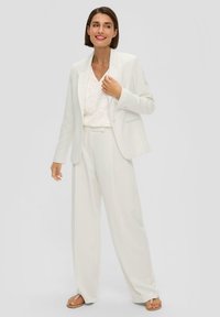 Biała, dopasowana marynarka i szerokie spodnie wykonane z lekkiego materiału, zestawione ze wzorzystą bluzką. Proste sandały dopełniają całość.