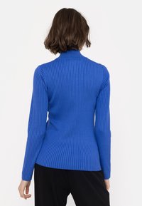 Blå ribbad långärmad tröja med hög hals och figurnära siluett, med en texturerad stickning och en lätt neddragen fåll baktill.