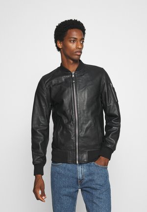 Blouson aviateur en cuir noir avec col et poignets côtelés, doté d'une fermeture éclair frontale et d'une poche latérale. Texture lisse et coupe ajustée.