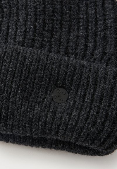 Tissu en maille côtelée gris foncé avec une petite étiquette métallique ronde noire embossée du mot "CLOSED" attachée près du bord.