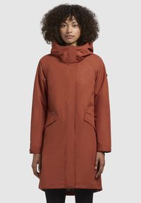 Abrigo de color óxido, resistente al agua, con capucha, que cuenta con bolsillos frontales y líneas limpias. Fabricado en material sintético con un acabado suave.