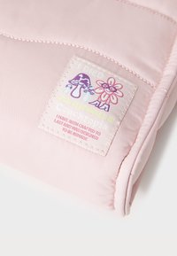 Tissu matelassé rose clair avec une surface texturée. Une étiquette brodée présente des illustrations colorées d'une fleur et d'un champignon, accompagnées de texte.