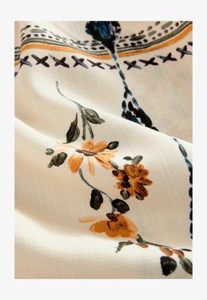 Tessuto a motivo floreale con sfondo bianco, caratterizzato da fiori arancioni e neri, foglie verdi e accenti blu, in una trama morbida e testurizzata.