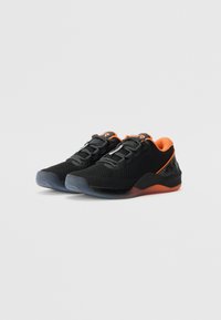 Czarne buty sportowe z pomarańczowym wnętrzem, czarno-szare sznurówki, teksturowane podeszwy i niskoprofilowy design, wyeksponowane na białym tle.