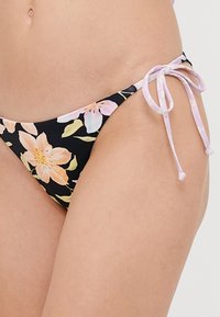 Cvetni bikini spodnji del z ravno črno podlago in pastelno cvetjem, dopolnjen s svetlo vijoličnimi vrvicami ob straneh. Eleganten material in minimalna pokritost.