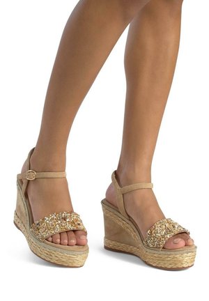 Beige wedge sandals with beaded straps, a woven jute sole, and a smooth suede upper. Features an ankle strap with a metal buckle.