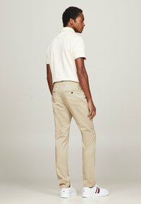 Chinos beige con una vestibilità slim e una polo blu classica. La polo ha una texture morbida e l'outfit è abbinato a sneaker bianche con accenti rossi e blu.