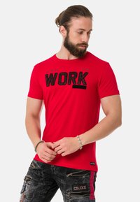 Rotes Baumwoll-T-Shirt mit einem auffälligen schwarzen "WORK"-Grafik, rundem Halsausschnitt und kurzen Ärmeln. Kombiniert mit strukturierten schwarzen Hosen.