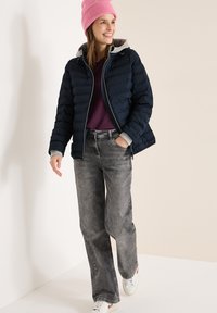 Doudoune bleu marine avec capuche grise, pull violet et jean à jambes larges gris. Bonnet en tricot rose. Chaussures décontractées à base blanche avec accents rouges.