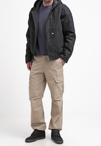 Black hooded jacket with a front zipper, tan cargo pants with multiple pockets, and black sneakers. Material appears durable, with a solid color scheme.