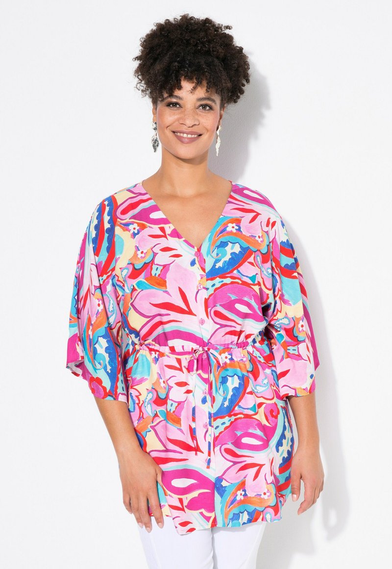 Tunic a stampa floreale colorata in rosa, rosso e turchese. Presenta un collo a V, maniche corte e una coulisse regolabile in vita.