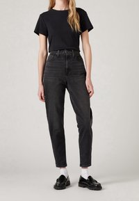 T-shirt in cotone nero abbinato a jeans in denim neri a vita alta, con una vestibilità rilassata e orli risvoltati. Mocassini neri e calzini bianchi completano il look.