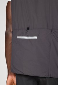 Dunkelgraue, leichte Jacke mit glatter Textur, ausgestattet mit einer Reißverschlusstasche und einem reflektierenden Akzentstreifen auf der Rückseite.
